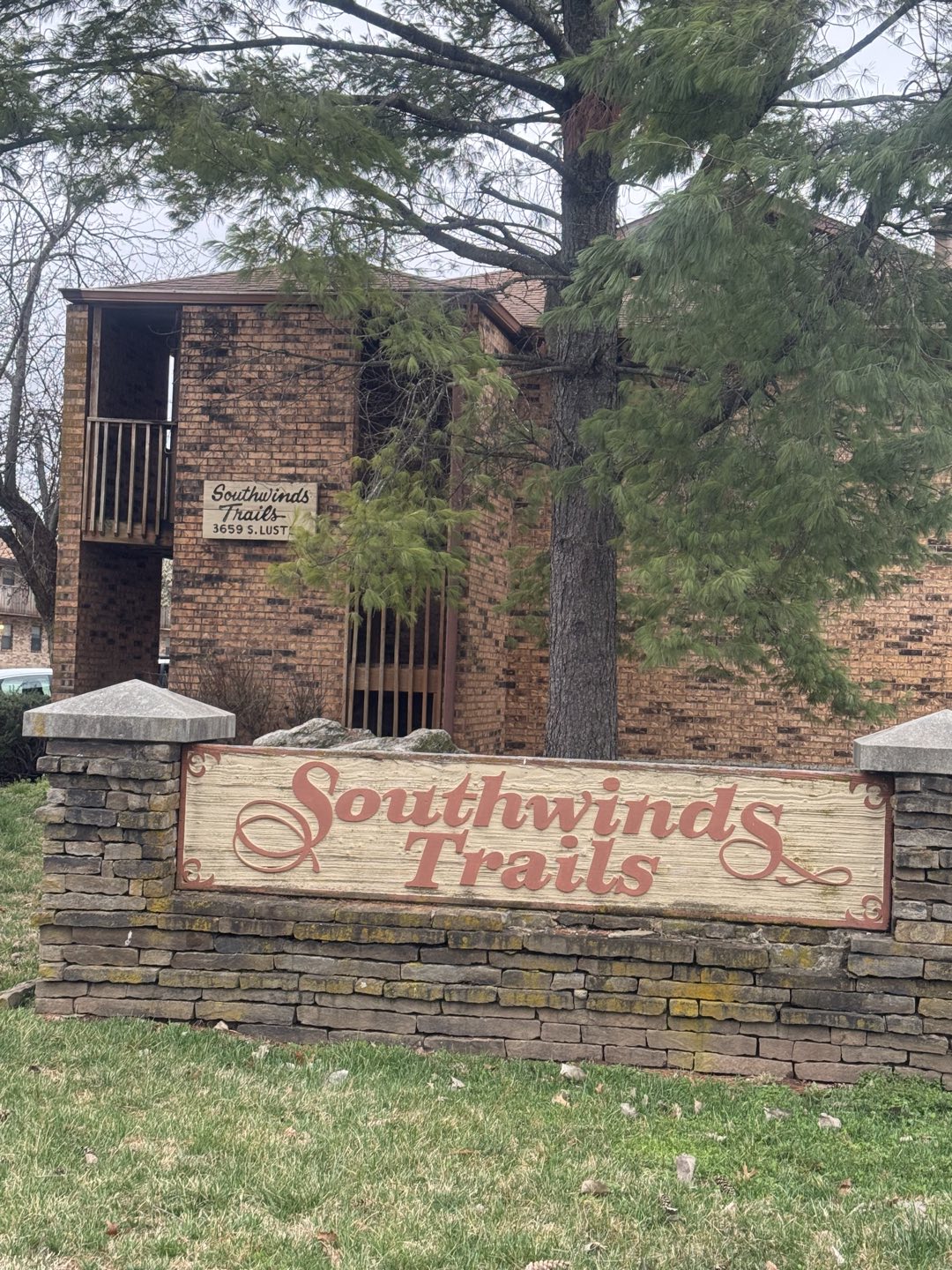Brick apartment building behind the carved wooden Southwinds Trails sign on a stone base